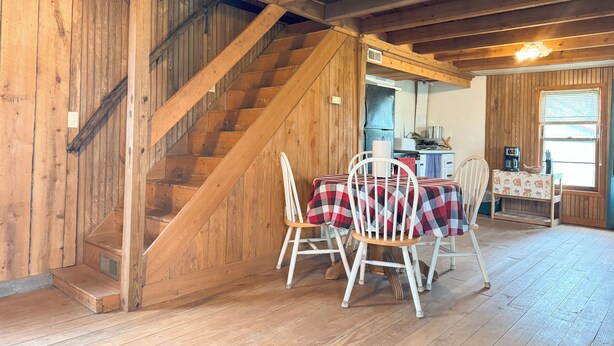 Een houten interieur met een trap, een eethoek met tafel en stoelen, en een keuken met apparatuur.