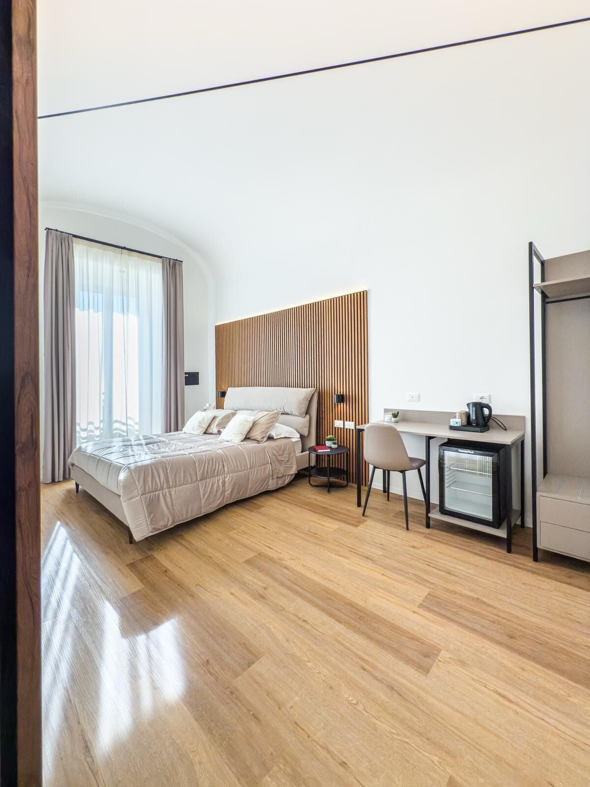 A modern hotel room with a bed, a desk, a chair, and a mini-fridge.