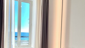 Una habitación con vista al mar a través de una ventana, un sofá con cojines y una lámpara de pie.