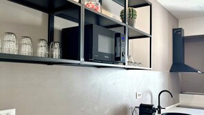 Una cocina moderna con armarios blancos, un microondas negro y una estantería empotrada con frascos de vidrio.