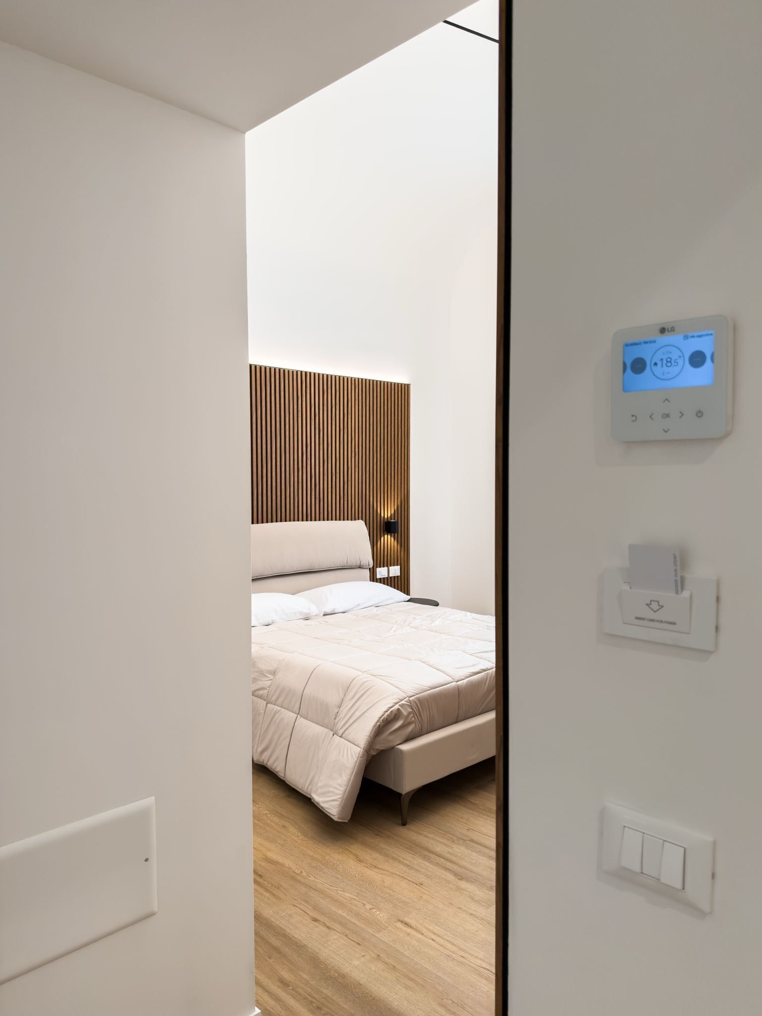 A modern bedroom with a bed, a wall-mounted thermostat, and a light switch.
