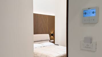 A modern bedroom with a bed, a wall-mounted thermostat, and a light switch.