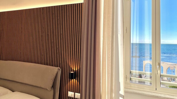 Un dormitorio con cama, una mesa redonda, un ventanal con vista al mar y una cortina.