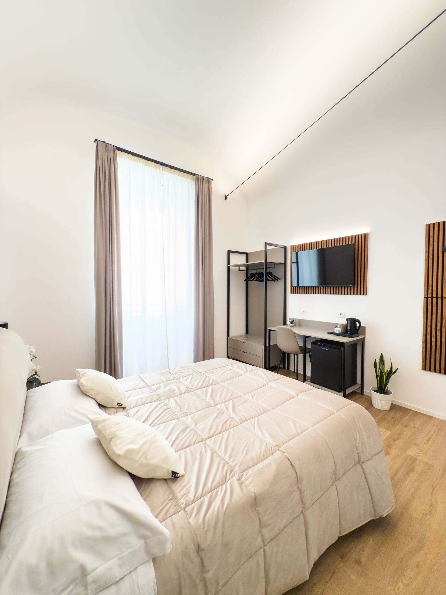 Une chambre d’hôtel moderne équipée d’un grand lit, d’un bureau, d’une chaise, d’une télévision et d’une petite plante.