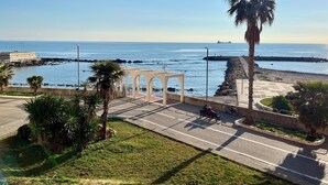 Un paseo marítimo con una palmera, un pabellón blanco y un banco.