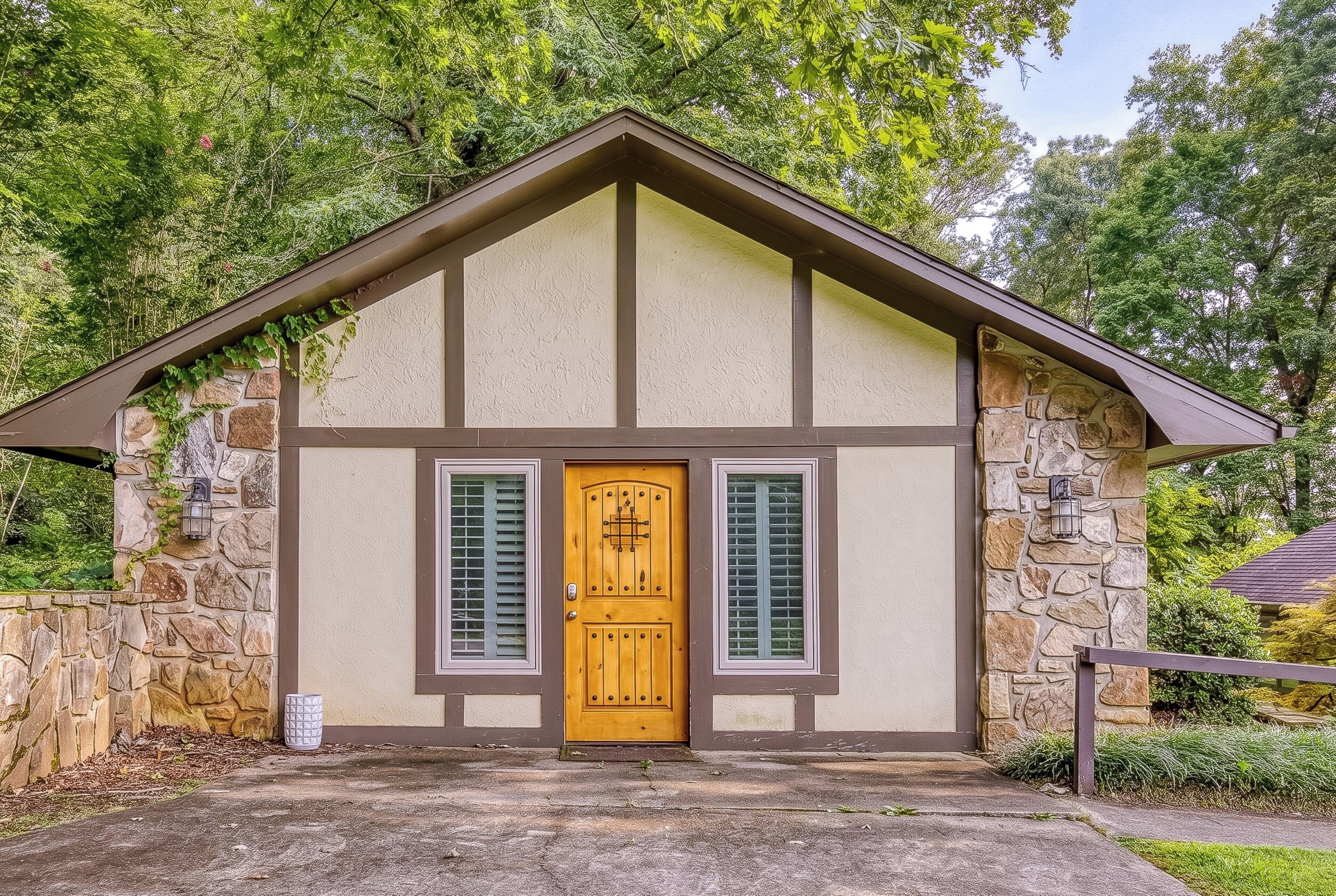 Un pequeño edificio de piedra con puerta y contraventanas de madera, rodeado de vegetación.
