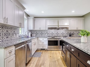 A modern kitchen with white cabinets, a patterned backsplash, stainless steel appliances, and a wooden floor.