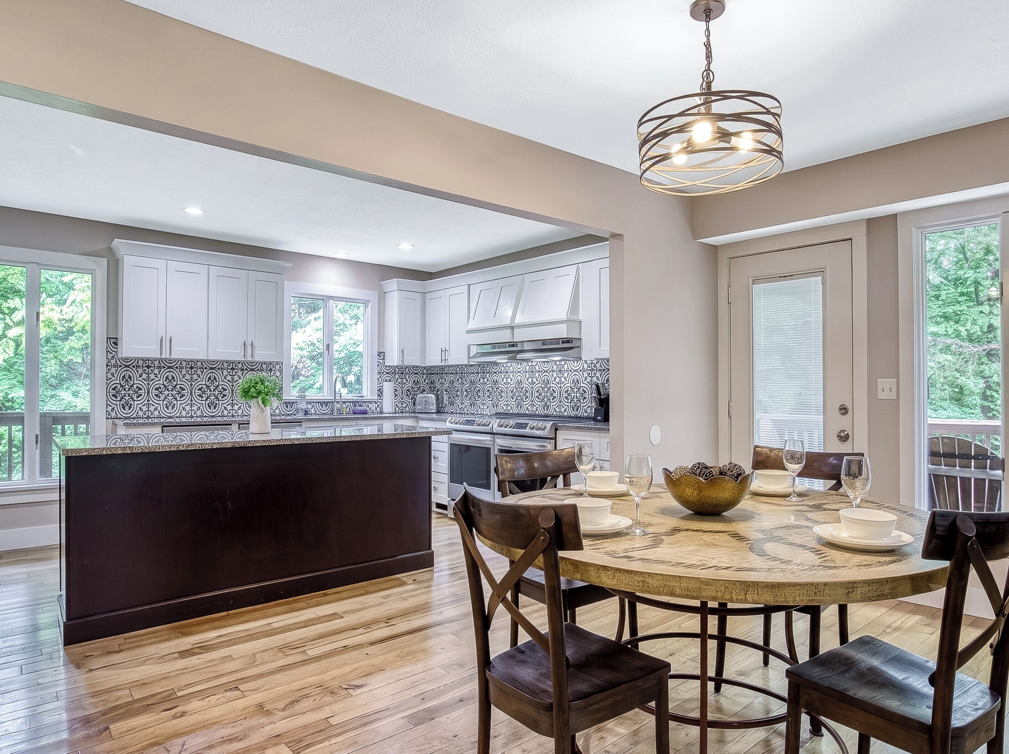Cocina moderna con armarios blancos, una isla negra y un comedor con mesa y sillas redondas.