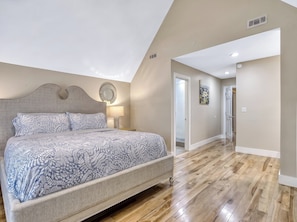 A bedroom with a bed, a bedside lamp, a wall clock, and a door leading to another room.