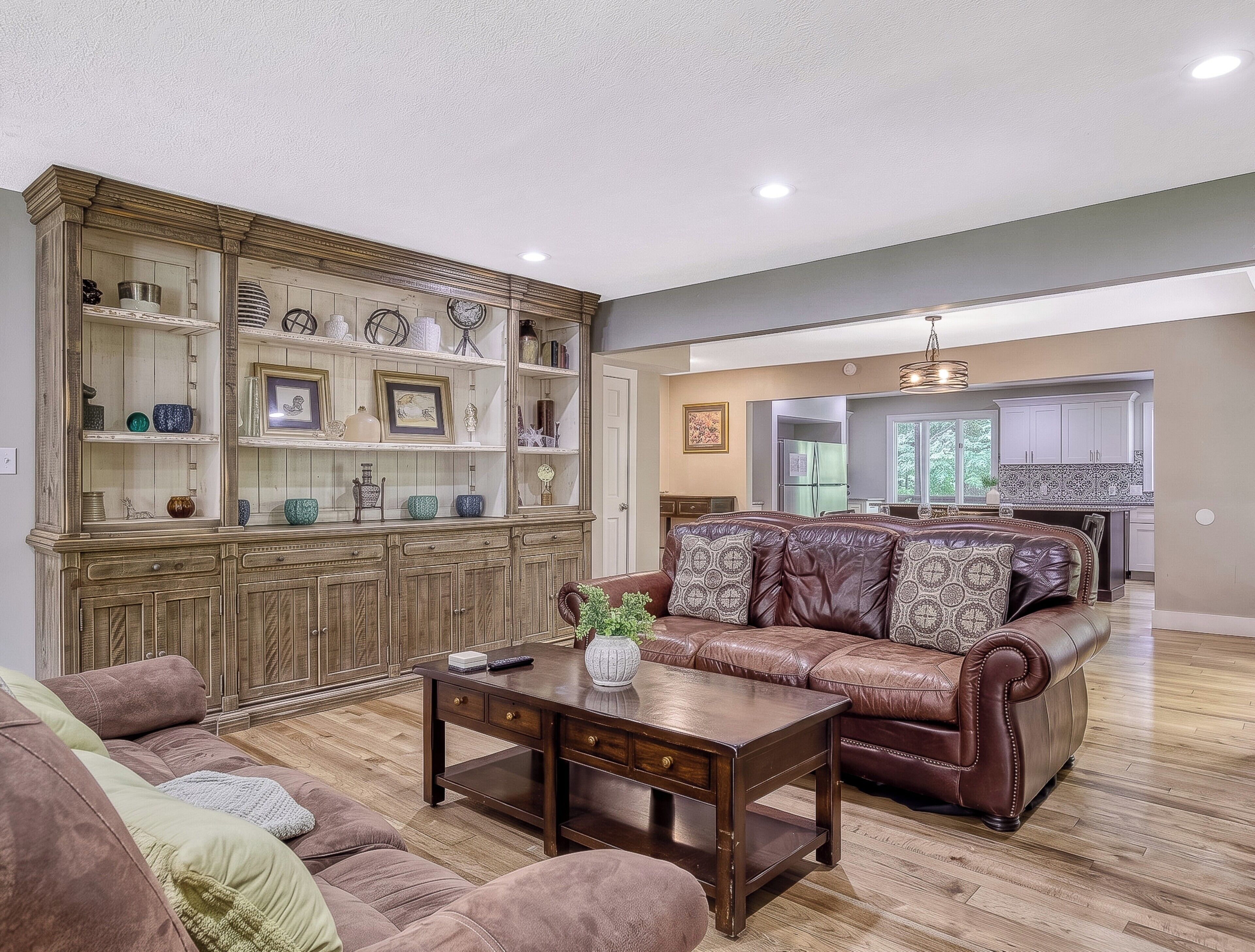 A living room with a brown leather sofa, a wooden coffee table, and a built-in wooden cabinet with shelves.