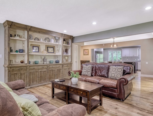 A living room with a brown leather sofa, a wooden coffee table, and a built-in wooden cabinet with shelves.