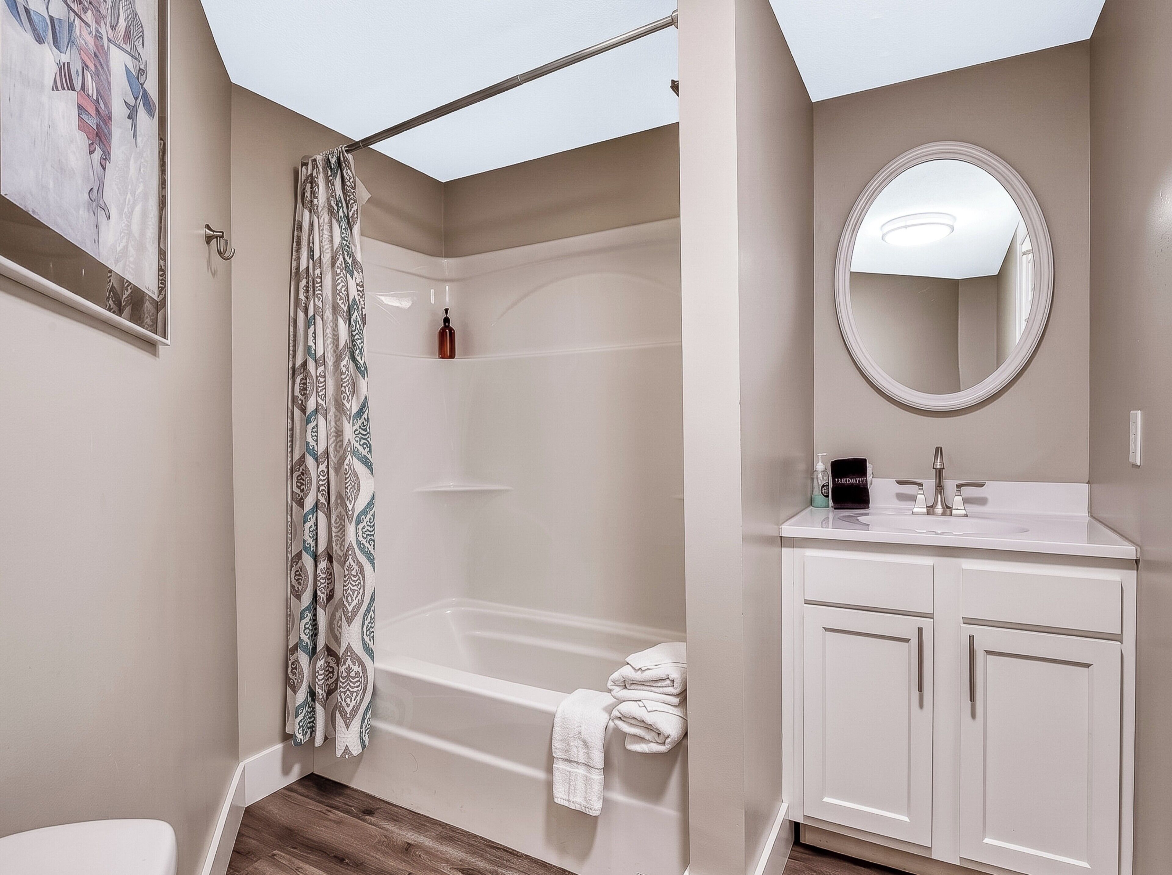 Un baño con bañera, inodoro, lavamanos con espejo y cortina de ducha.