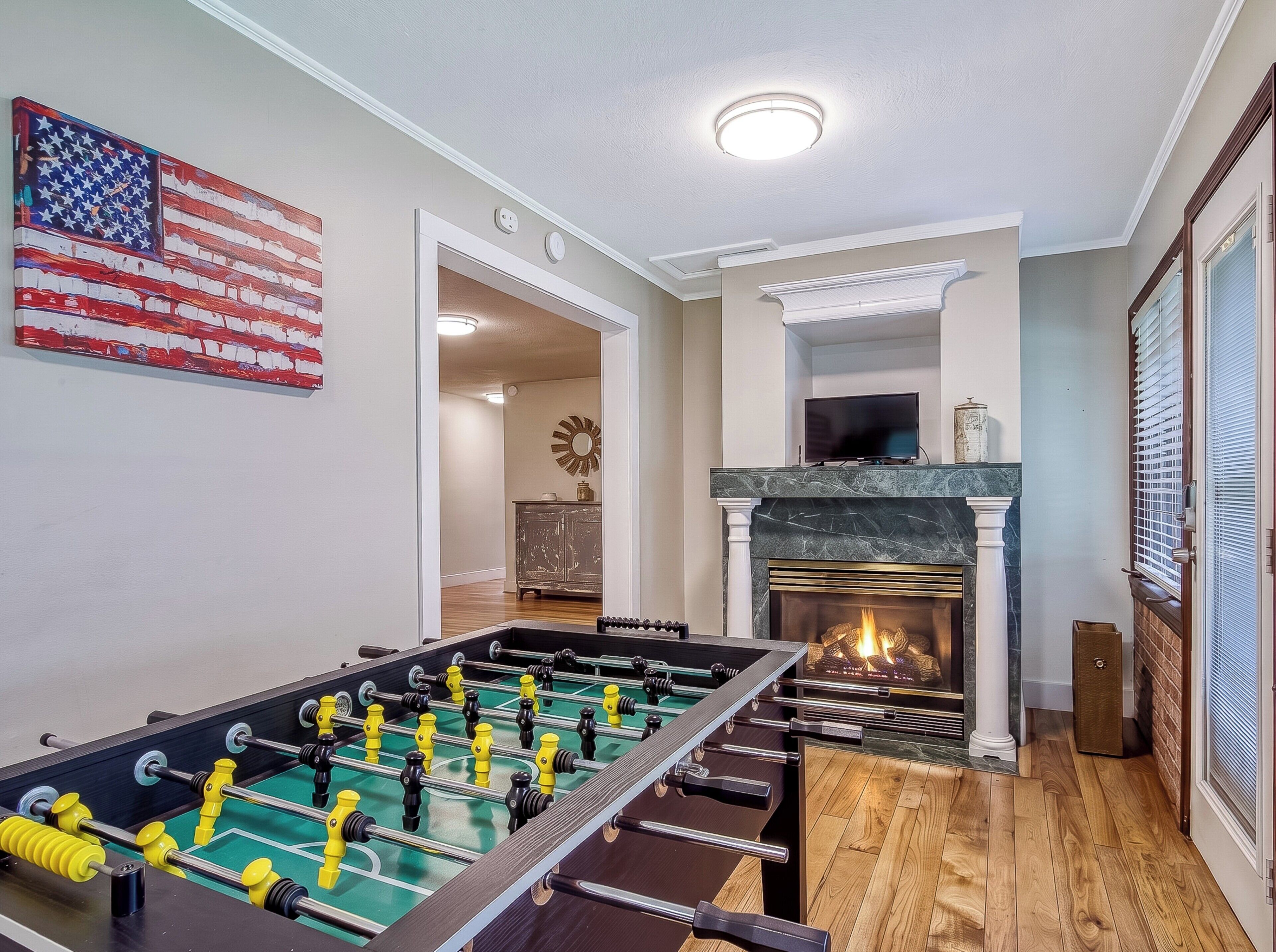 Une pièce avec une table de baby-foot, une cheminée et un drapeau américain accroché au mur.