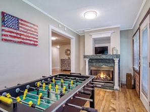 A room with a foosball table, a fireplace, and an American flag on the wall.