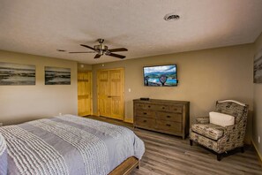 Ein Schlafzimmer mit einem Bett, einem Schminktisch, einem Sessel, einem Deckenventilator und einem Fernseher an der Wand.