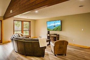 A living room with a curved sectional sofa, a television mounted on the wall, and a wooden floor. - Big Bear Lodge | Sleeps 28 | Mtn Views + Hot Tub (Sevierville)