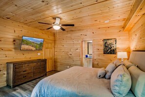 A wooden cabin bedroom with a bed, dresser, ceiling fan, and artwork on the walls. - Big Bear Lodge | Sleeps 28 | Mtn Views + Hot Tub (Sevierville)