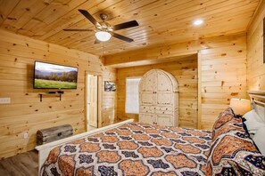 Ein Schlafzimmer einer Holzhütte mit einem Bett, einem Deckenventilator, einem Fernseher und einem Kleiderschrank.
