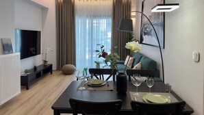 A modern living room with a dining area, featuring a flat-screen TV, a sofa, and a dining table set for two.