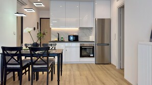 A modern kitchen with white cabinets, a stainless steel refrigerator, and a dining area with a table and chairs.
