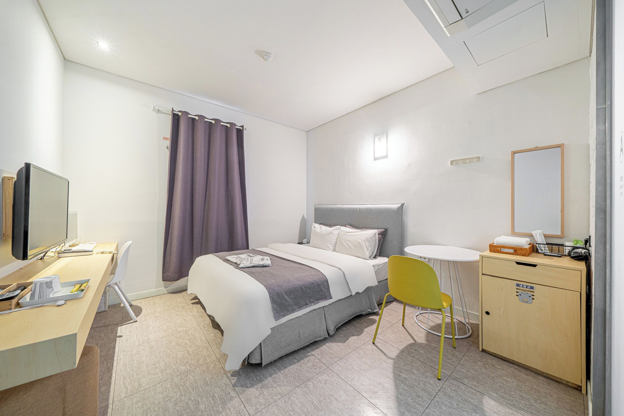 Una habitación de hotel moderna con cama, escritorio, silla y un mueble pequeño.