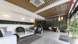 Een moderne woonkamer met een bank, stoelen, een salontafel en een open haard. Er staan potplanten en een groot raam zorgt voor natuurlijk licht.
