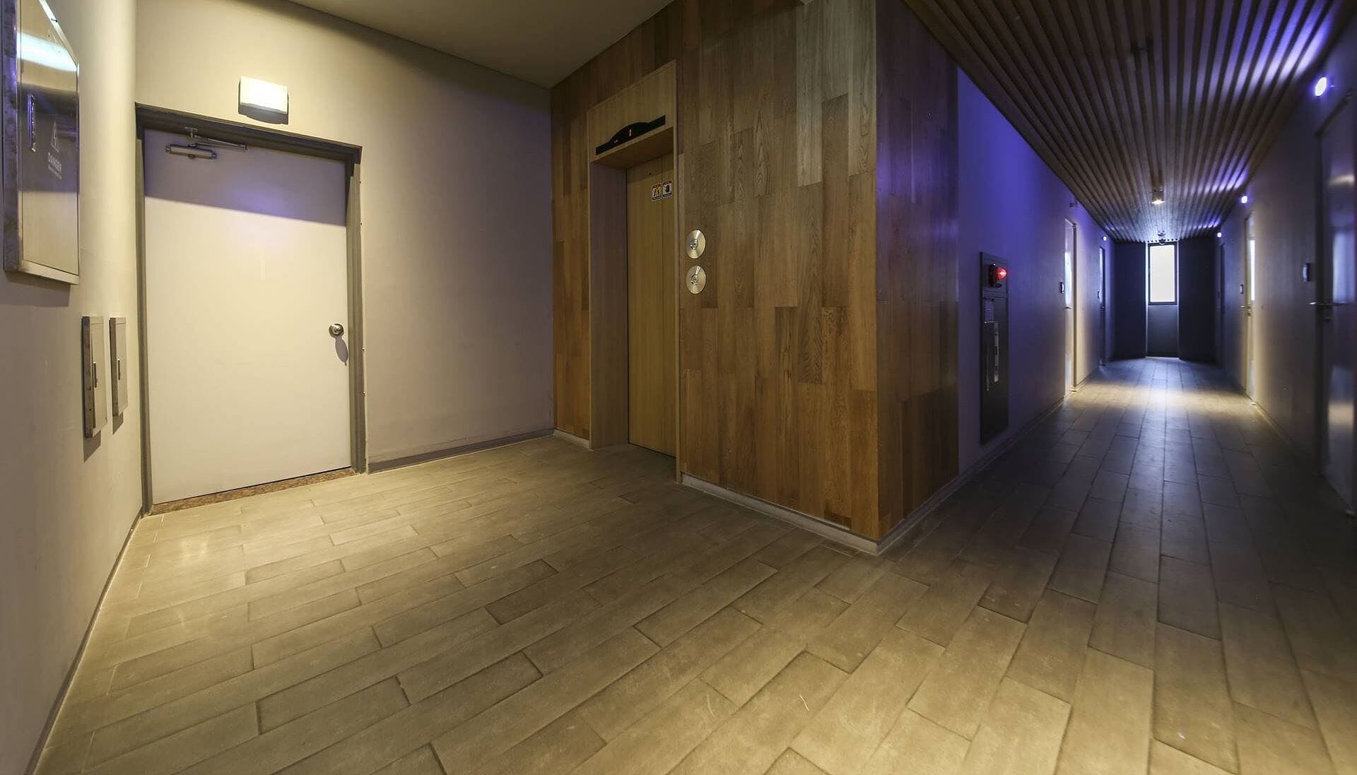 Een gang met houten vloer, een deur met lichtschakelaar en een inbouwlift.