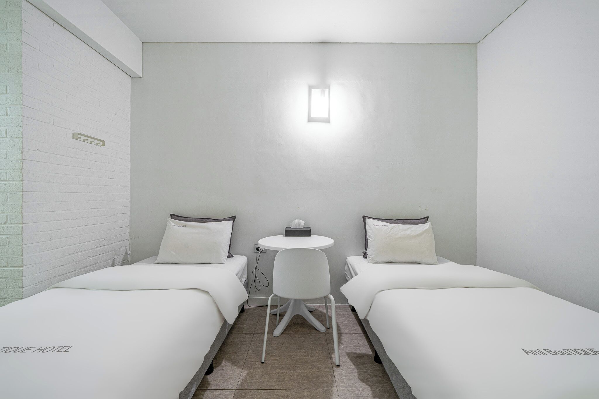 A small, clean room with two single beds, a small round table, and a chair.