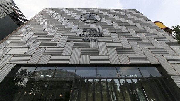 Het exterieur van het Ami Boutique Hotel met een modern architectuurontwerp, met een opvallend 'Ami'-logo en borden voor het hotel en café.