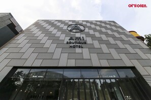 Das Hotel Ami Boutique zeigt sich von außen mit einem modernen architektonischen Design, inklusive des gut sichtbaren 'Ami'-Logos und Schilder für Hotel und Café.