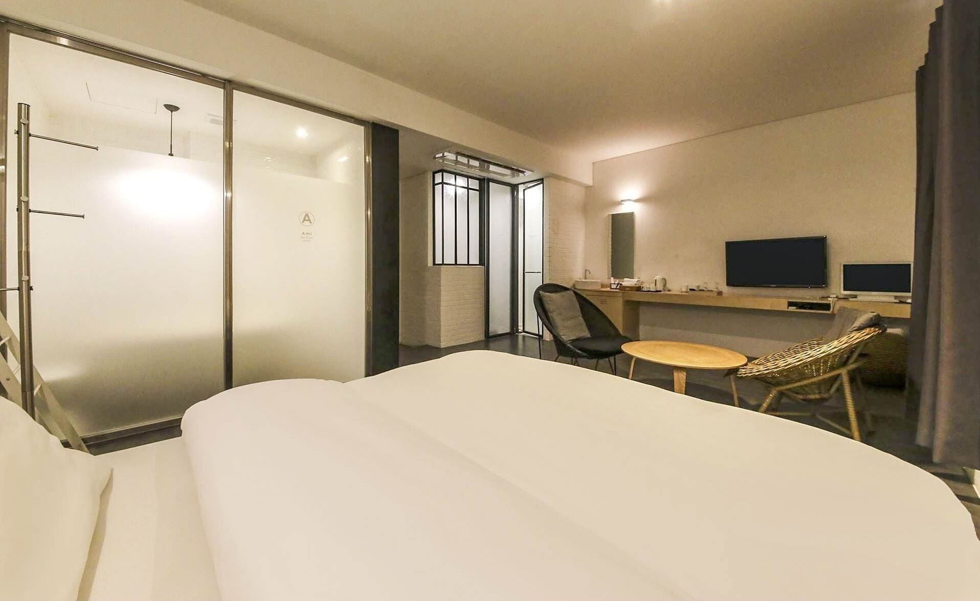 A hotel room with a bed, a desk with a chair, a TV, and a window.