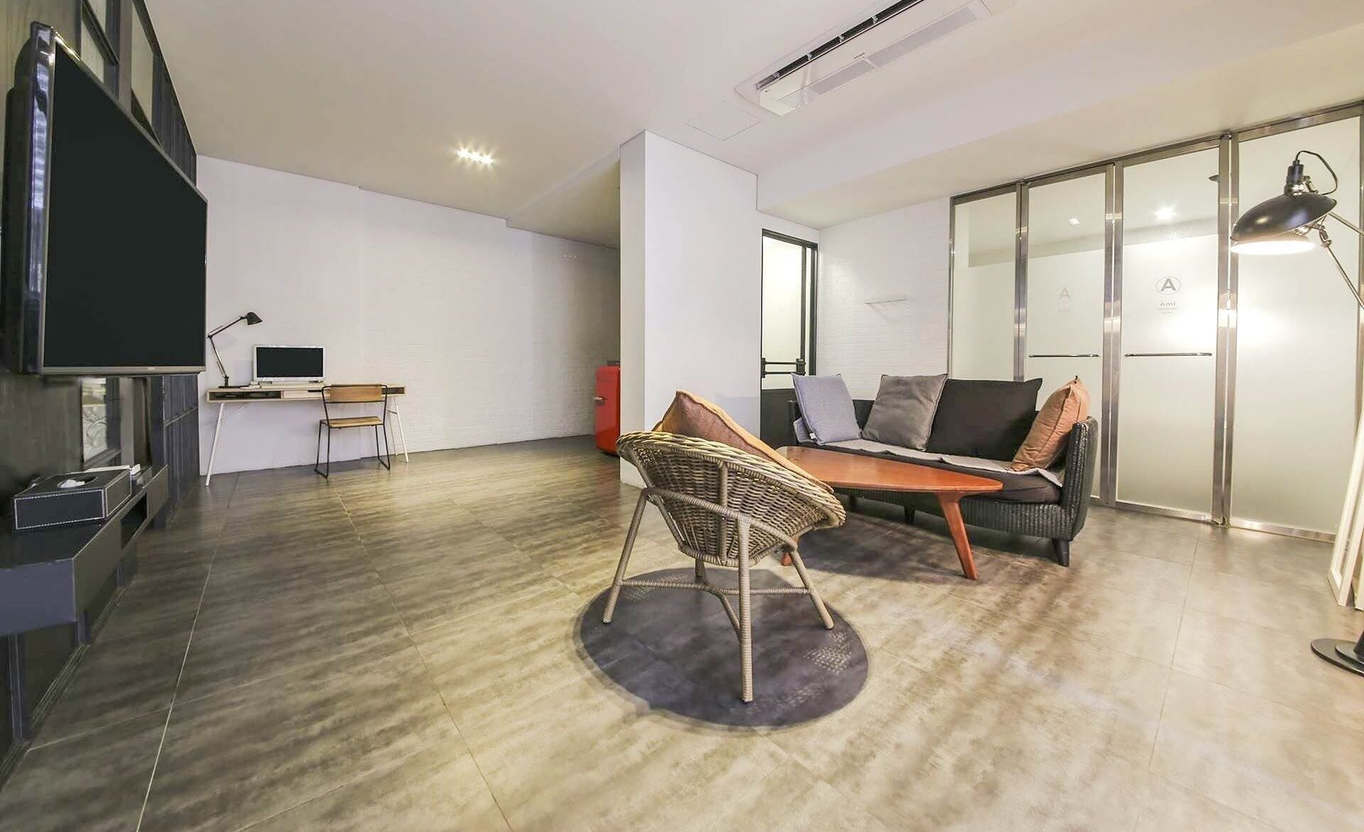 A modern living room with a sofa, a wicker chair, a small table, a TV, and a desk with a computer.