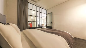 Een hotelkamer met een groot bed, een raam met jaloezieën, een stoel en een kleine tafel.