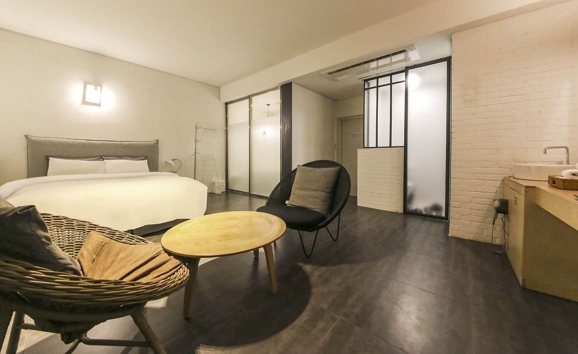 A modern hotel room with a bed, a small round table, a chair, and a desk with a sink.