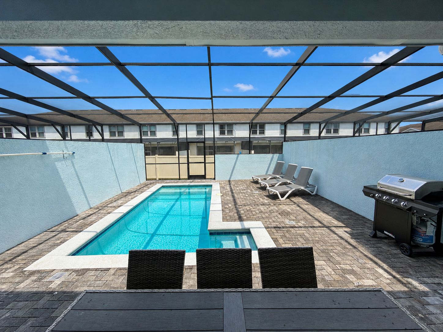 A rooftop pool with a clear view of the sky, a barbecue grill, and lounge chairs.