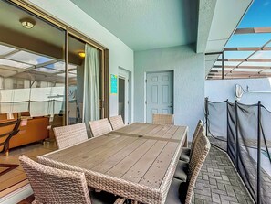 An outdoor patio with a wooden table and wicker chairs, a sliding glass door, and a view of the sky.