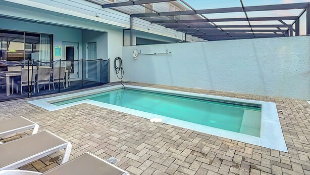 Une piscine avec une terrasse en briques, un espace salon couvert et un bâtiment doté d’une fenêtre et d’une porte.
