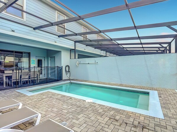A swimming pool with a brick patio, a covered seating area, and a building in the background.