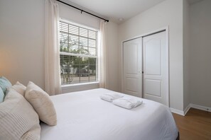 Ein Schlafzimmer mit einem Bett, Kissen, einem Fenster mit Jalousien und einer Tür.