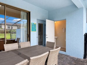 Ein überdachter Patio-Bereich mit Tisch und Stühlen, eine Tür, die zu einem Badezimmer führt, und ein Plakat mit den Poolregeln an der Wand.
