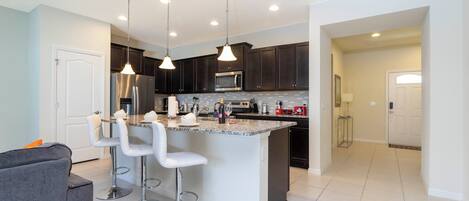 A modern kitchen with dark cabinets, a central island with bar stools, stainless steel appliances, and pendant lighting.