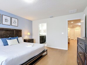 A bedroom with a bed, bedside table, lamp, and framed pictures on the wall.