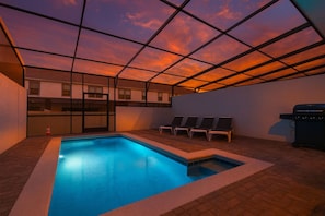 Ein Pool auf dem Dach mit Blick auf den Sonnenuntergang, Liegestühle und ein Grill.