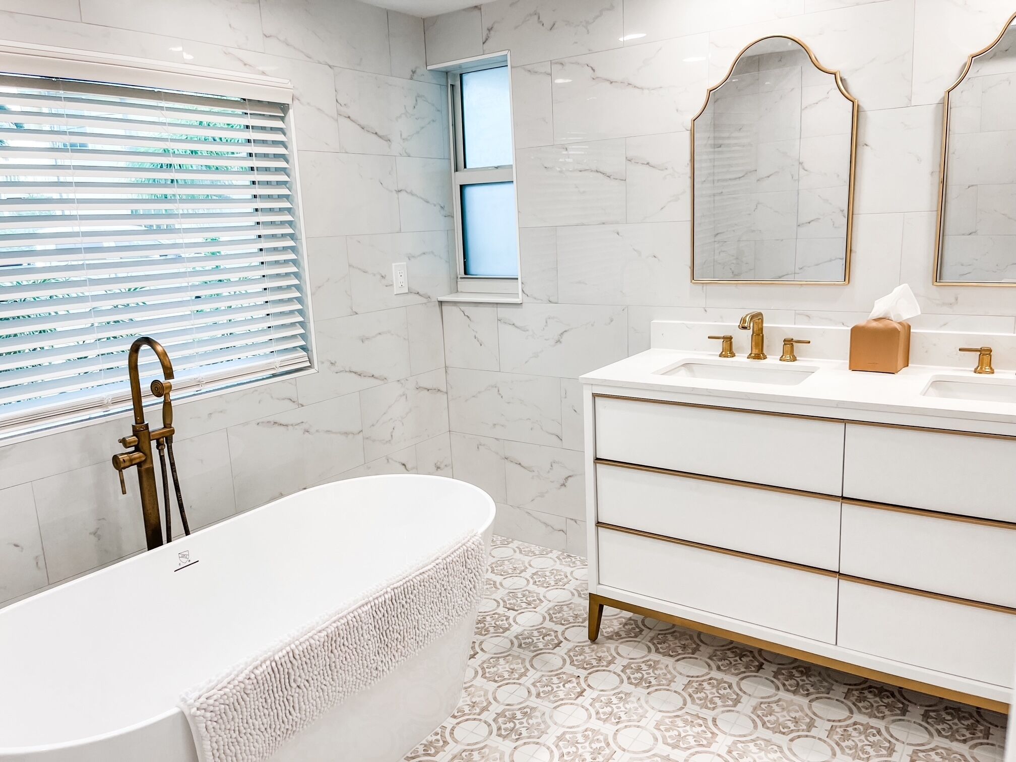A modern bathroom with a freestanding bathtub, a vanity with gold fixtures, and marble walls.