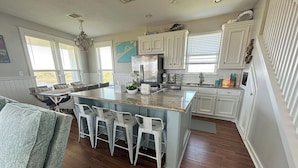 A spacious kitchen with white cabinetry, a central island with bar stools, and a dining area with a table and chairs.