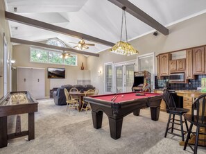 A spacious living area with a pool table, a foosball table, and a dining area with a large window providing natural light.