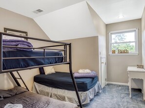 A dormitory room with bunk beds, a desk, and a window with a view.