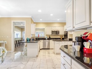 A modern kitchen with white cabinetry, a central island, stainless steel appliances, and a marble floor.