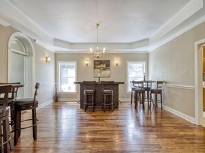 A spacious dining area with a bar, wooden flooring, and a chandelier.