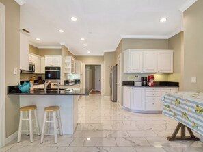 A modern kitchen with white cabinetry, a marble floor, and a central island with stools. - Bella Vista, Perfect for Groups,  Indoor Pool, 12,000 Sq. Ft !!! (Sevierville)